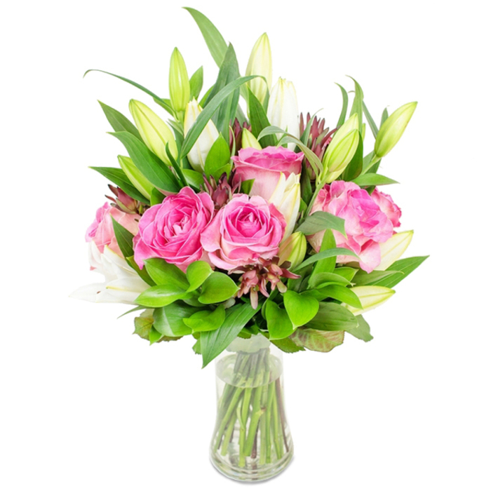 A carefully balanced floral composition presented in a clear glass vase, photographed against pristine white to emphasise every petal and leaf. The focal point is a cluster of fully opened deep pink roses, their velvety layers presenting rich fuchsia and soft blush tones that catch a diffuse, even light. White lily buds are artfully placed among the roses; many remain closed or only just unfolding, their tapered, green-tinged exteriors promising the arrival of trumpet-shaped, luminous white interiors. Surrounding the flowers is abundant greenery: broad, glossy leaves provide a sculptural backbone while smaller, tender sprigs add a finer, shimmering texture. Subtle, darker burgundy or reddish-brown flecks-small buds or accent foliage-are threaded through the bouquet to create depth and a gentle visual anchor against the brighter flowers.
The vase is transparent and modestly tapered, holding clear water in which the green stems are visible and neatly trimmed. The overall silhouette is full and dome-like, the arrangement demonstrating careful proportion and rhythm between bloom and foliage. In describing this arrangement to someone who cannot see it, one would note the cool freshness suggested by the clear water, the silky softness of the rose petals, and the poised restraint of the lily buds. This bouquet carries the atmosphere of a quiet celebration-suitable for anniversaries, Mother's Day, or as a thoughtful centrepiece for a home in Mill Hill Village or near Bittacy Hill-offering a combination of visual richness and subdued elegance.