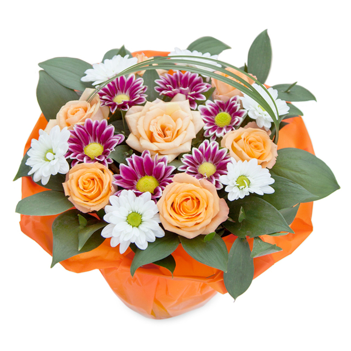 Photographed from a gentle overhead angle to capture every nuance, this exquisite bouquet from Flowers Mill Hill reveals the meticulous work of seasoned North London florists. Bold, fully bloomed roses in soft peach and cheerful orange command the eye from the center, their velvet petals swirling in creamy gradients and recalling the tranquil trails around Mill Hill Park. Meanwhile, compact clusters of white daisy-like chrysanthemums with verdant green centres evoke the resilient wildflowers of Arrandene Open Space, while vibrant magenta and purple chrysanthemums inject an exuberant dash of colour, their petals framing lively lime-green disks. Deep, luscious foliage surrounds the floral mosaic, each leaf gleaming with a healthful shine-adding both structure and a whisper of the woodsy aromas found along Frith Lane. The contemporary silhouette is completed by a single arc of bear grass, effortlessly poised over the top, introducing a whisper of modern elegance and continuity. Bound together, the bouquet is finished in bright, beautifully wrinkled orange paper, a final flourish that both protects and highlights the design's artistry. This joyful showpiece, perfect for anniversaries, celebrations, or welcoming a new season, offers an evocative glimpse into the natural beauty and creative craftsmanship of Mill Hill's local flower scene.