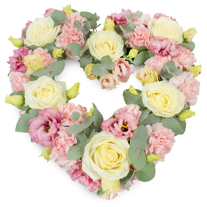 This photograph captures a beautifully composed heart-shaped wreath, an elegant funeral tribute that balances soft pastel tones with graceful greenery. The heart itself is flawlessly formed, with smooth curves and a defined inner cleft, every inch covered in flowers so that the arrangement appears rich, full, and thoughtfully finished. Large cream and pale yellow roses are placed as key focal points around the heart, their velvety petals spiralling from the centre like quiet, unfolding memories. Each rose is open yet structured, suggesting tenderness and enduring devotion. Between these, generous clusters of light pink carnations create a frothy, textured backdrop, their finely ruffled petals layering one upon another to create a sense of comforting softness, like a gentle embrace. Scattered throughout the design, deeper pink to mauve lisianthus blooms introduce a more saturated note of colour, their open, bell-shaped petals and subtle shading offering visual depth and emotional resonance, much like the changing light over the rooftops of Mill Hill. Tiny yellow-green buds, some just beginning to open, add small sparks of freshness and quiet hope. Silvery-green eucalyptus leaves weave all through the wreath, their round, smooth surfaces and muted hue lending a cooling presence that frames and supports the blooms, giving the heart clear definition. The flowers and foliage together create a palette of blush pinks, creamy whites, soft lemons, and gentle greens, producing an atmosphere of peace, remembrance, and heartfelt sympathy. Expertly crafted by local Mill Hill florists, this heart-shaped arrangement feels perfectly suited for funeral services, memorial gatherings, or to accompany a final farewell at a nearby cemetery or crematorium, expressing deep love and respect without the need for many words.