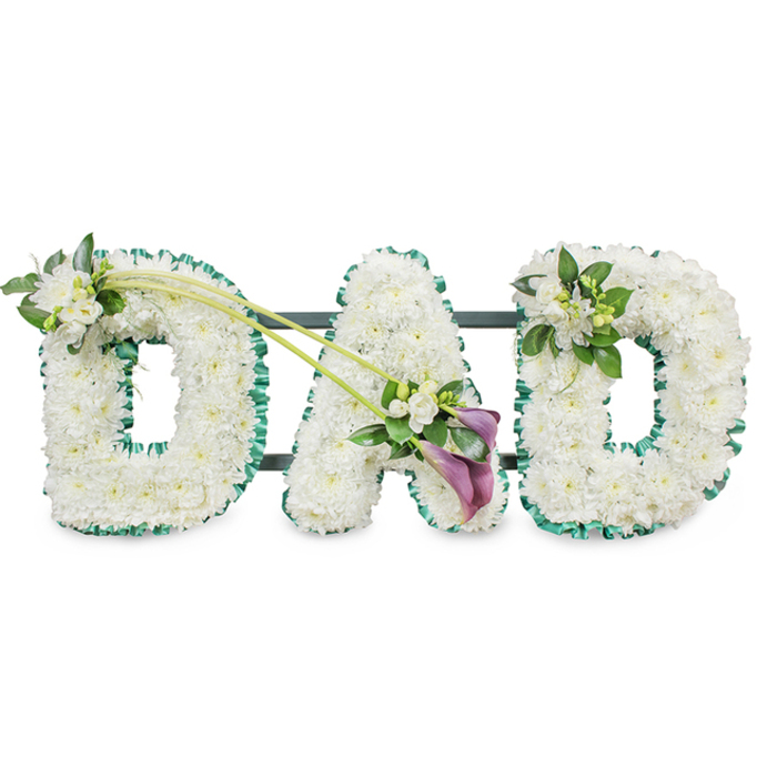 A beautifully composed funeral tribute spells out the word DAD in three large, three-dimensional block letters, the sort often chosen by families in Mill Hill to honour a much-loved father. Each letter is expertly covered in countless white chrysanthemums, or similar small button flowers, arranged tightly so that the petals touch and overlap, creating a thick, plush cushion of blooms. Their snowy whiteness conveys purity and remembrance, while the soft, rounded shapes of each flower head lend a gentle, comforting feel to the strong, upright capitals. Along the outer edge of every letter runs a rich emerald green ribbon, lightly ruffled, its satin surface catching the light and providing a striking outline to the flowers. The contrast between the cool white petals and the vivid green border evokes the calm of nearby green spaces in Mill Hill, such as the fields and tree-lined walks the area is known for. Behind the letters, faint hints of a dark frame reveal the sturdy structure that allows the tribute to stand upright as a single, unified piece.   

The florist has added thoughtful touches of extra flowers and foliage to enhance the design without overshadowing the simple, powerful word. On the upper left arc of the first D, a dainty cluster of white freesia blossoms and rich greenery is nestled among the chrysanthemums, their slender buds and open bells adding depth and a light, sweet scent. From this point, two long, graceful green stems sweep diagonally across to the central A, visually linking the first two letters. At the lower right of the A, the stems culminate in an elegant, asymmetrical spray: two deep purple or maroon calla lilies, with their sculpted trumpet shapes, are arranged among more white freesia and fresh leaves, introducing a deeper, more contemplative colour accent. The final D carries a coordinating yet slightly more compact spray of white freesia and foliage on its upper right curve, echoing the first letter and bringing balance to the composition.   

Set against a bright, uncluttered white background, this DAD tribute communicates love, respect, and profound loss in an understated but deeply moving way. It is a fitting choice for funerals, memorials, or cremation services throughout Mill Hill, offering families a visually clear and emotionally resonant way to say goodbye.