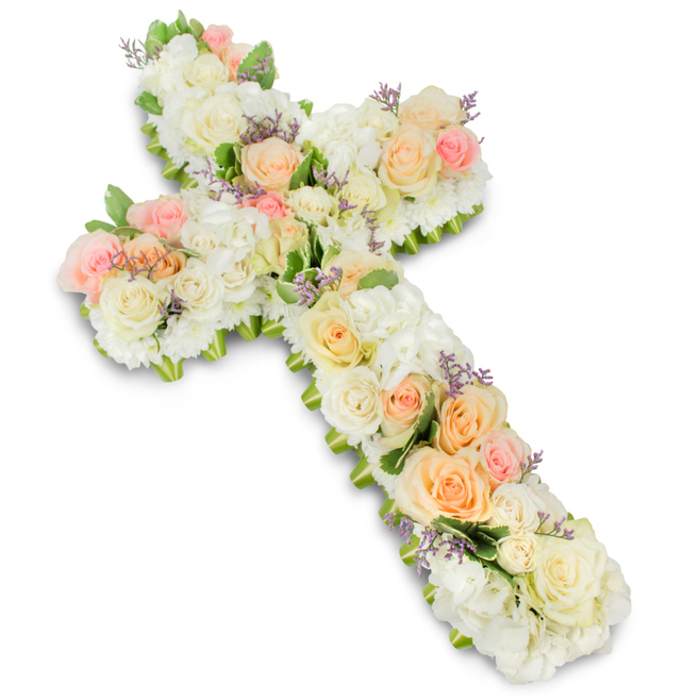 An elegant floral cross, designed as a sympathy tribute, stands out clearly against a crisp white background, its quiet colours and abundant blooms telling a story of remembrance and faith. The cross is solidly built from flowers alone, with each part of the Christian symbol covered in petals that gently soften its lines. At the centre of attention are premium roses in creamy white, ivory, soft peach, and light blush pink, arranged in thoughtfully placed clusters along the vertical and horizontal arms. Their open, layered petals create a romantic, soothing texture that feels both refined and deeply personal, as if each rose represents a cherished memory. Around and between these focal roses, mounds of white hydrangea or similar dense blossoms fill the structure, creating a thick, pillowy base that adds volume and luxurious softness. Smaller white spray roses and compact filler flowers nestle into every remaining space, making the entire surface look plush and complete, with no visible mechanics. Scattered delicately throughout are small touches of lavender or pale purple filler blooms, which introduce a hint of gentle colour contrast while maintaining the overall pastel harmony. Slight glimpses of fresh green foliage appear at the edges and beneath some of the blossoms, helping to define the shape of the cross and adding a whisper of garden freshness that would feel at home in Mill Hill's leafy residential streets. The lighting is soft yet bright, casting a faint shadow underneath that gives the tribute depth and presence. This floral cross would be beautifully suited to a church aisle, crematorium chapel, or memorial setting in Mill Hill, conveying peace, respect, and the hope of eternal rest for a loved one.