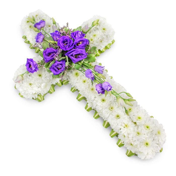 A carefully crafted floral cross, intended as a sympathy or funeral tribute, lies in stillness against a glowing white background that places the entire focus on its flowers. The cross is made up almost entirely of densely grouped white spray chrysanthemums. Each small flower has gently cupped petals that overlap with its neighbours, composing a dense, velvety blanket of white. At the centre of each chrysanthemum, a soft green eye adds a hint of colour, creating a delicate speckled effect that brings the surface to life. Running neatly along the sides of the cross, a narrow lime-green ribbon or trim has been applied with precision, framing the arms and stem and lending the piece a fresh, contemporary edge without disturbing its traditional symbolism. The focal point sits at the intersection of the cross: a generous cluster of deep purple lisianthus blooms. Their ruffled, bell-shaped flowers are layered in rich, velvety folds, from inky violet depths to slightly lighter purple edges, giving the arrangement a sense of depth and quiet luxury. Intermingled with these lisianthus are fine sprigs of greenery, a few tiny filler flowers, and closed buds that hint at blooms yet to open. From this central spray, several lisianthus flowers and buds drift down along the lower right arm, forming a graceful, diagonal cascade that adds movement and elegance. Soft studio lighting casts only a faint shadow under the cross, making it appear as though it gently rests on a white surface in a calm Mill Hill workshop. The overall mood of the design is one of serene faith and tender remembrance, suitable for a service at a local church off Flower Lane or as a dignified tribute at a graveside gathering nearby.