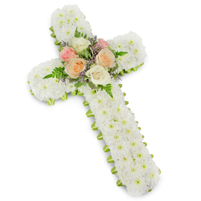 A solemn yet beautifully composed floral cross is shown in full, centred on a pristine white background that amplifies its serene character. The entire face of the cross-both the long vertical beam and the shorter crossbar-is densely paved with small white button chrysanthemums. Each bloom is tightly packed, with almost no space between petals, producing a plush, velvety texture that reads as one continuous field of white. This uniform covering gives the cross a calm and balanced appearance, symbolising purity, spiritual peace, and the comforting presence of faith during a time of mourning. Following the perimeter of the cross is a slender band of lime green ribbon, applied in a clean, unbroken line. Only a narrow edge of the ribbon shows, just enough to frame the design and create a gentle contrast that recalls the fresh greenery of the gardens and open spaces dotted around Mill Hill. At the centre where the two beams meet, the monochrome white surface is gently interrupted by a small, artfully arranged cluster of roses. These roses, fully opened and soft in tone, range from creamy ivory to delicate blush pink and gentle peach. Their rounded, layered petals form a tender focal point. Around and between them, feathery fern fronds and small lavender or soft purple filler flowers add texture, movement, and a whisper of colour. The arrangement looks meticulously balanced, as if created by an experienced local florist with deep understanding of funeral traditions. Intended for use as a tribute at a service, wake, or graveside within the Mill Hill community, this floral cross offers a thoughtful expression of sympathy, remembrance, and everlasting love.