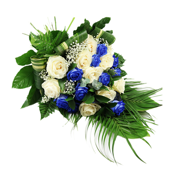 A luxurious cascading spray of blue and white roses lies against a clean white background, its form shaped into a long, elegant teardrop that widens at the upper left and gently narrows as it stretches towards the lower right. The composition is dense, with numerous large rose blooms touching and overlapping to create a lavish, textural surface. The blue roses are a vivid sapphire, almost jewel-like, and are thoughtfully scattered among an equal number of creamy ivory and soft white roses so that the eye travels evenly across the arrangement. Each rose appears freshly opened, its velvety petals unfolding in spirals that catch subtle highlights and shadows. Nestled between the roses, sprays of white baby's breath add a fine, clouded softness, as if a light mist had settled over the flowers. The entire spray is framed and supported by an abundant array of foliage. Deep, glossy leaves gather along the top and left side, anchoring the design, while fresh, bright green fern fronds reach upward and outward, giving an airy, feathery texture. From the lower right, long dark green palm fronds extend and arc, defining the cascading silhouette and creating a sense of gentle movement, like the slow descent of leaves in the quiet gardens around Mill Hill. Here and there, subtle sprigs of bluish-green, eucalyptus-like foliage introduce cooler tones and a distinctive rounded leaf shape. Some of the broader leaves have been expertly folded or wrapped to form horizontal bands and elegant loops, adding a structured, contemporary note to the otherwise soft and organic spray. This carefully balanced design suggests reverence, peace, and enduring love, ideal as a prominent sympathy tribute at a funeral, memorial service, or graveside gathering in Mill Hill and neighbouring areas.