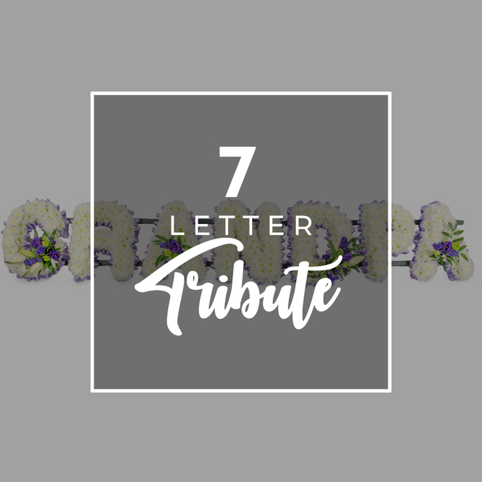 A calm, even grey backdrop forms the setting for this thoughtful memorial image, where every detail has been composed with care. Dominating the centre is a dark charcoal-grey square, edged with a fine white border that sets it subtly apart from the background. Within this square, white typography introduces the concept of the piece: a bold numeral 7 sits at the top, followed by the word LETTER in a smaller, straightforward sans-serif font, and then Tribute written in a graceful, cursive style. This text clearly signals a personalised seven-letter funeral tribute. Just behind this panel, running horizontally through the frame and partially concealed, is a floral name arrangement that spells GRANDAD. Each letter is constructed from a solid bed of pristine white chrysanthemums or similar compact blooms, packed closely together so that no gaps are visible. The resulting texture is plush and velvety, creating a sense of softness that contrasts gently with the crisp lines of the central square. Dotted throughout the white flowers are accents of rich purple blossoms-perhaps lisianthus or miniature roses-interwoven with fresh, bright green foliage. These touches of colour are placed with intention along the curves and corners of the letters, adding dimension and a natural, garden-inspired feel without distracting from the purity of the white base. The design suggests the kind of bespoke funeral letter tribute crafted by a skilled Mill Hill florist for services held at local churches, crematoria, or cemeteries, or for delivery to family homes along the leafy avenues near Mill Hill East. The word GRANDAD carries a strong emotional weight, and this arrangement translates that affection into a serene, beautifully composed floral farewell.