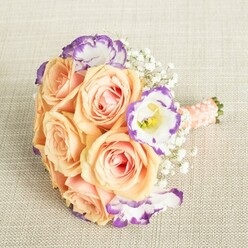 In the soft, ambient light of a Mill Hill home, this artfully assembled bouquet lies serenely against a textured ivory cloth-an art piece in bloom. At its heart, plush roses glow in apricot and peach, their layered petals evoking the warmth of summer afternoons in Mill Hill Park. Interlaced between them, brilliant white Lisianthus with expressive purple-edged petals offer a vibrant contrast, reminiscent of the creative flair found drifting through Mill Hill East's weekend markets. Wispy clusters of Baby's Breath lend an ethereal, gossamer effect, their cloud-like presence stitching together the arrangement in a seamless dance of tradition and innovation. The bouquet's stems are tightly hand-tied and finished with a lustrous peach-pink satin ribbon, detailed with luminous pearls-a nod to enduring wedding customs and the trustworthy craftsmanship of local Mill Hill florists. Whether destined for a cheerful bridal procession down The Broadway or as the centerpiece for elevating a family milestone, this bouquet embodies the spirit of Mill Hill with its delicate hues and thoughtfully balanced composition. Every bloom, texture, and carefully chosen ribbon enriches the bouquet's story-a modern creation rooted in timeless celebration and local pride, ideal for anyone seeking to mark a special moment in this beloved North London community.