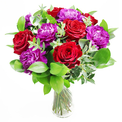This arrangement offers a captivating play between bold colour and soft texture, uniting deep red roses with lavish purple peonies in a harmonious display. The roses are the defining shapes, each flower open and expansive, with velvety petals spiralling confidently outward from the centre. Intermixed with them, the peonies provide a looser, more cloud-like form; their many ruffled petals gather into rounded blooms that feel indulgent and full. The whole cluster of flowers emerges from a supportive base of greenery: rich, dark green leaves curve outward like a natural frame, while slender stems of eucalyptus trail through and beyond the blooms, their pale, silver-green discs adding airiness and dimension. The clear glass vase that holds the bouquet is understated and modern, allowing a clear view of the neatly gathered stems and the clean water, which catches subtle reflections of light. It is easy to imagine this bouquet sitting in a bright room of a Mill Hill house or apartment, perhaps near Mill Hill East station, where afternoon light would make the reds glow richly and the purples take on a gentle, almost satiny sheen. The imagined fragrance is one of understated luxury: sweet, romantic notes of rose laced with the refreshing, slightly citrus scent of eucalyptus, akin to a breath of fresh air drawn on a walk across the open spaces of Arrandene or Mill Hill Park. Ideal for marking significant moments-a promotion, an anniversary dinner, or a heartfelt thank-you-this bouquet conveys thoughtfulness and a quiet sense of occasion that resonates with the calm, village-like feel of Mill Hill.