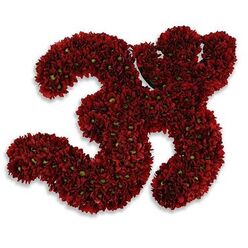 A handcrafted floral homage shaped into the sacred Om symbol, composed entirely from deep red chrysanthemum blooms, offers a quiet, devotional presence on a stark white field. Each blossom is packed with care so that the rich, velvety petals form continuous swirls and counters of the symbol, the deep garnet tone recalling ripe autumn fruits and hearth-side warmth. Tiny lime-green centres peek from within many of the button chrysanthemums, providing a gentle, living contrast that gives the Om its subtle articulation and natural punctuation. The white ground intensifies the crimson and makes the curves read clearly at a distance, while a soft, cool grey shadow beneath suggests the piece sits slightly raised, almost as if the offering hovers with reverent calm. Close to the work, you would notice the faint, earthy scent of freshly cut chrysanthemums - a grounding aroma that steadies the spirit and lends this composition its comforting, contemplative mood. The craftsmanship is evident in the even density of the packing and the seamless way the petals flow into symbol-shaped negative space; it reads as both a floral sculpture and a sacred offering. In Mill Hill this kind of tribute is familiar in community gatherings and private ceremonies, lending comfort at a village hall or a quiet family observance near Mill Hill Village or Mill Hill Park. The piece is less about ornament and more about presence: a visual prayer that holds room for grief, solace, and respectful remembrance rendered with the attentive hand of an experienced floral maker.