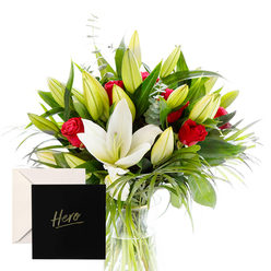 From the workshop at Flowers Mill Hill, this bouquet is a portrait of sophistication and emotion, carefully composed to evoke admiration and comfort. The white lilies, large and trumpet-shaped, stand like generous beacons among abundant green spears and curls of foliage. Red roses cluster passionately throughout the composition, their fragrance mingling with the lilies in a dewy, hypnotic aroma that carries through a Mill Hill living room on a sunlit afternoon. The abundance of unopened buds promises beauty yet to come, offering a sense of hope and ongoing celebration for someone who inspires you. The natural arrangement gleams in bright, clear light, each leaf and petal outlined with freshness, as if just gathered from a morning garden stroll along The Green or near Mill Hill Broadway.

Presented with a card marked Hero, this creation becomes more than a bouquet; it is a thoughtful expression of thanks or remembrance-a floral embrace for a neighbour, teacher, colleague, or someone whose spirit genuinely inspires. The bouquet rests in a simple glass vase, the stems bound with discreet twine, allowing the lilies and roses to breathe while the greenery provides a soft, forest-like backdrop. Flowers Mill Hill takes care to balance scale and texture, so the scent travels gently, not overpowering, perfect for an intimate celebration or a moment of quiet reflection. For families and friends across Mill Hill seeking a heartfelt gesture, same-day delivery is available, ensuring freshness and personal touch from our local team.