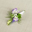 A delicately crafted wedding boutonniere rests on a softly textured light beige linen background, the neutral fabric allowing every petal and stem to stand out with quiet elegance. At the heart of the design are two open lisianthus blooms, their creamy white petals edged with a rich, royal purple that ripples along the ruffled contours like ink along handmade paper. Nestled close are tiny white filler flowers that echo the lightness of baby's breath, adding a misty, cloud-like softness between the bolder blooms. Threading vertically through the centre, a slim spike of deep purple muscari, or grape hyacinth, introduces a line of tight bell-shaped florets, their cool tone deepening the overall palette and suggesting the freshness of an early spring morning in Mill Hill Park. Fine, feathery greenery, similar to asparagus fern, fans gently around the flowers, bringing movement and a touch of wild garden charm, while a pair of pale green, unopened buds hint at blossoms still to come. The stems are neatly gathered, carefully aligned, and wrapped in smooth white satin ribbon, the fabric folded and tied into a small, precise bow that signals it is ready to be pinned onto a lapel for a wedding at a Mill Hill synagogue, a prom, or a formal celebration at a nearby country club. The overall mood is refined yet natural, as though it could have been picked from a well-tended garden just off Mill Hill Broadway, capturing both the romance of the occasion and the thoughtful craftsmanship of a local florist who understands the subtle power of understated detail.