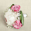 This carefully composed bouquet rests on a pale, slightly textured fabric background, reminiscent of the elegant linens often seen in Mill Hill reception rooms, and is photographed from a gently raised angle so every detail is visible. At the heart of the design lies a single, luxurious creamy white peony, its dense layers of petals opening like a down-filled cushion, creating a sense of depth and softness. Flanking it are two striking pink roses, one above and one below, their tightly whorled centers spiralling out into petals that shift from soft blush to vibrant fuchsia at the tips, adding a romantic burst of colour. Fine, branching stems of baby's breath weave between the larger blooms, their clusters of tiny white flowers scattering light and giving the bouquet a delicate, misty veil. Encircling the base, broad dark green leaves have been folded and curved with precision to cradle the flowers, their glossy surface offering a rich contrast to the matte softness of the petals. The stems are neatly gathered and wrapped in smooth white satin ribbon, forming a clean, comfortable handle that suggests this bouquet is designed to be carried for a wedding, engagement, or special celebration. Gentle lighting caresses the arrangement, enhancing the creamy tones of the peony, the rosy hues, and the deep greens, while soft shadows create a subtle sense of dimension. This image captures the thoughtful craftsmanship of a skilled Mill Hill florist, evoking scenes of brides walking through Mill Hill's leafy streets or couples exchanging vows in local chapels, with flowers that feel freshly gathered and lovingly arranged for their day.