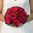 With an aura of timeless romance, this bridal bouquet becomes a vibrant centrepiece against the backdrop of a Mill Hill celebration. A profusion of deep red roses, rich in their velvety beauty and evocative of enduring devotion, gathers closely together, creating a lush tapestry of colour and texture. Tiny clusters of scarlet hypericum berries, glistening amongst the roses, scatter playful brightness and textural intrigue. All are edged by a structured collar of glossy, dark green leaves-imparting a sense of nature's architecture and echoing Mill Hill's green open spaces. Held securely in hands adorned with subtle, polished nails, the bouquet is accentuated by the sheer elegance of a lace-embellished white gown draping softly to one side. Soft, natural light highlights each detail, immersing the viewer in a gentle sensory experience where scent, colour, and tactile promise converge. This image mirrors the joyful energy of Mill Hill's nuptial traditions-a fresh and unforgettable floral arrangement perfect for couples tying the knot throughout Mill Hill and beyond.