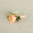 Presented from a high, intimate angle, this boutonniere centres on a single apricot-peach rose whose petals curl inward like a secret and open outward with velvety grace. The colour moves from a warm, sunlit apricot at the core to softer peach and cream at the edges, catching light in a way that makes the petals look almost silk-soft beneath fingers. Surrounding the rose, clusters of tiny white baby's breath provide a soft, cloud-like contrast that breathes lightness into the piece, while slender, vivid green blades of grass weave through for contrast and motion. Two deeper green leaves have been folded into delicate loops behind the flower, adding a quiet architectural note and natural depth. The stems are bound in matching peach satin ribbon, precisely wrapped and tied into a small, refined bow; the ribbon's sheen complements the bloom and suggests a smooth, tactile finish. Close to the stem wrap a subtle metallic pin or wire peeks through-practical and discreet-ready for a groom's lapel or a prom jacket. The boutonniere rests on light beige, cross-hatched linen that softens the scene and evokes the calm textures of Mill Hill Village markets and weekend craft stalls. As a local floral artisan piece from Flowers Mill Hill, this boutonniere reads as intentional and intimate: a small talisman of affection, freshly scented and crafted to sit gracefully through vows, photographs, and first dances across the Mill Hill area.