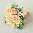 There is a quiet clarity to this bridal arrangement, a composition that reads like a gentle love letter in peach and white. At its heart sit creamy peach roses, their petals layered in soft spirals that reflect a candlelit or early-morning glow, each bloom shaped with the kind of careful selection we practise at Flowers Mill Hill. Surrounding them, clouds of tiny white gypsophila float like mist, their minute blossoms scattering the light and giving the bouquet a delicate, fairy-like edge. Darker, glossy greenery-broad leaves and thin, textured stems-anchors the design so the soft peach appears brighter and more tactile. The handle is swathed in peach satin ribbon, smoothed and folded until the wrap feels as luxurious as the blooms themselves; along the seam a string of small pearls is secured, their subdued sheen suggesting tradition and an intimate family heirloom. The scent is subtle: a cool, leafy note underlined by the faint sweetness of the roses, reminiscent of a spring morning on a route from Mill Hill Broadway toward the village shops. Held in the hand, the bouquet is light and balanced, designed for a bride who prefers quiet confidence to showy drama. I can see it complementing a classic lace gown or resting gently on a reception table, the gentle palette lending itself to both church and garden ceremonies. As a local florist I think of it as an emblem of refined simplicity-an arrangement that honours vows with softness, poise and everyday beauty.