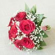An elegant bouquet of red roses and white baby's breath rests on a soft, cream-coloured fabric, the muted background allowing every detail of the flowers to shine. At the heart of the composition, a compact cluster of deep crimson roses-about six or seven blooms-forms a rounded dome, each rose fully opened so that its velvety petals create layered spirals of rich red. The roses are surrounded by a generous scattering of gypsophila, or baby's breath, whose tiny white blossoms gather in fine clusters, producing a mist-like effect that softens the intensity of the central blooms. Around the lower edge of the bouquet, glossy dark green leaves emerge just enough to frame the flowers, lending structure and a refreshing, garden-like feel without drawing attention away from the roses. The stems are neatly brought together and wrapped in a vivid red ribbon, forming a smooth handle that would sit comfortably in the hand of a bride or someone giving a romantic gift. Along the ribbon, a line of small, pearl-style dots winds in a gentle spiral, adding a subtle sparkle and suggesting a special occasion. Beneath, the off-white fabric-slightly textured like linen or canvas-provides a calm, neutral base. The overall impression is of a traditional, romantic bouquet, ideal for a wedding in Mill Hill, perhaps carried from a home near Mill Hill Park to a ceremony at a nearby venue, or delivered locally to celebrate anniversaries, proposals, or meaningful moments shared across NW7.