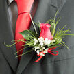 The composition of this Mill Hill boutonnière marries classic romance with thoughtful detail, just the sort of finishing touch a groom might choose after a calm consultation at Flowers Mill Hill. At the heart of the design is a beautifully shaped hot pink rose, its petals curling protectively around the centre like a gentle embrace. The rose's colour is lively and affectionate, glowing warmly against the dark fabric of the suit lapel. Encircling the bloom are fluffy clusters of baby's breath, each white flower tiny yet distinct, creating a whispered contrast that speaks of purity, constancy, and quiet joy. Delicate, feathery grasses sweep around the rose in soft arcs, lending the boutonnière a subtle sense of movement, reminiscent of grasses stirring in the breeze on a walk through Mill Hill's open green spaces. A single, glossy, deep green leaf backs the arrangement, its smooth, waxy surface catching hints of light and providing a clean, structured silhouette. At the base, a refined red ribbon is tied neatly, adding a discreet note of colour that echoes the pink tones and underscores the celebratory mood. The overall impression is one of freshness and intention, a compact design that feels carefully edited rather than overworked. You can almost sense the faint, sweet fragrance of the rose blending with the green notes of the foliage, as if the flowers had just been cut and assembled moments before the ceremony. Perfect for weddings, anniversaries, or formal gatherings around Mill Hill Broadway and nearby venues, this boutonnière expresses beauty in the smallest details and the quiet confidence of a well-planned occasion.