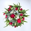 Viewed from directly above against a spotless white background, this abundant bouquet forms a generous, almost perfectly circular cluster of colour and texture. At its centre, deep crimson red roses draw the eye, some still in tight bud and others beginning to unfurl, their velvety petals layered like little whirlpools of romance. Nestled beside them are rich fuchsia and ruby red carnations, their ruffled, full blooms adding a playful, festive energy that feels ideal for a joyful celebration in Mill Hill. Between these warmer tones, clusters of dainty white spray chrysanthemums and other small daisy-like blossoms punctuate the arrangement with crisp brightness, giving the bouquet a clean, uplifting feel, like fresh air after rain on Mill Hill Park. Tiny florets of white gypsophila, or baby's breath, float delicately in the gaps, softening every edge with a cloud-like haze that makes the whole design appear light and airy despite its density. All of this colour is carefully framed by layers of lush greenery: broad, pointed dark green leaves, likely from lily or alstroemeria stems, create a strong architectural base, while rounded, silvery-green eucalyptus leaves weave through, adding cool sophistication and modern charm. The lighting is even and natural, allowing each tone of red, white, and green to stand out in vivid detail without harsh shadows. The bouquet feels like a thoughtfully composed gift, perfect for an anniversary, birthday, or heartfelt get-well message delivered to a doorstep off Mill Hill Broadway. Its mood is one of warmth, vitality, and affection, as though each bloom has been chosen to say, You are cherished, in a language of petals and leaves.
