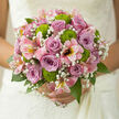In this romantic wedding bouquet, the flowers are arranged with the same quiet care you might feel wandering through the greener corners of Mill Hill. At the heart, dusky mauve and lilac roses create a rounded focal point, their petals unfurling in tight, velvety spirals that suggest trust, tenderness, and enduring partnership. Threaded among them, fine sprays of gypsophila add a whisper-soft texture, like tiny white stars scattered through the arrangement, blurring the transitions between each bloom. Bright green button chrysanthemums nestle playfully between the roses and filler flowers, their domed shapes and vivid chartreuse colour injecting freshness and a hint of modern flair. Around the central blooms, pink alstroemeria spread outward in gentle arcs, their slim petals flaring slightly at the tips and adorned with delicate natural markings, lending the bouquet movement and a feeling of openness. A frame of rich greenery envelops the entire design, the leaves smooth-edged and slightly glossy, offering contrast in both colour and texture while keeping the silhouette rounded and balanced. The neatly bound stems create a comfortable handle, perfect for holding during a ceremony at a Mill Hill church or registry office and later during photographs taken along Mill Hill Broadway. Soft, even daylight washes over the bouquet, illuminating the cool pastels, bright greens, and snowy whites, and giving the impression of freshly cut flowers just arranged by an experienced local florist. The overall effect is one of quiet joy and refined celebration-a bouquet that feels as though it was designed to cradle heartfelt wishes and mark a meaningful new chapter.