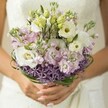 Soft, early morning light and the natural beauty of Mill Hill come together in this ethereal bridal bouquet. Cupped in a bride's hands, the bouquet glows with creamy white Lisianthus, their ruffled petals gently unfurling around sunny yellow-green centers. Wisps of pale green buds and clusters of pink-lavender stock weave through the bouquet, infusing it with airy texture and light fragrance, reminiscent of wildflower walks beside the Dollis Brook. The striking foundation is a dramatic band of deep purple, spiky Allium, providing modern contrast and structure-its geometry as captivating as the local Mill Hill gardens. Dark green bear grass loops gracefully through the midsection, tying the design together with contemporary elegance. The bride's nails, painted in subtle blush tones, encircle the wrapped stems, while the blurred suggestion of an ivory gown frames the scene softly in the background. This bouquet, a fresh expression of love from Flowers Mill Hill, blends delicate romance with refined London style, ideal for wedding celebrations and joyful gatherings in and around Mill Hill's picturesque NW7 community.