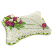 A rectangular, pillow-shaped funeral cushion is shown here, its surface entirely covered with a dense bed of pristine white chrysanthemum florets that read as a soft, cloud-like carpet under gentle studio light. The compact chrysanthemums create a plush texture you can almost feel beneath your fingertips - cool, velvety, and quietly soothing - while a delicate scalloped trim of lime-green satin ribbon frames the perimeter, adding a whisper of colour and a neat, pleated finish. In the upper left corner a rich cluster of deep magenta roses gathers like a small, dignified bouquet; their velvety petals open slowly, contrasted with tiny white freesia or lisianthus blooms tucked between them, lending faint citrus and creamy floral notes to the visual scent of the arrangement. Fresh emerald fern fronds and bright green leaves cradle the roses and form a lush backdrop, giving the piece dimensional depth. Across the white cushion two or three slender dark-green bear-grass blades arc diagonally from the top right toward the middle left, introducing graceful movement that guides the eye from the focal cluster toward the opposite edge. Near the upper right, a single matching magenta rose echoes the main cluster and balances the composition with subtle elegance. Set against a clean white background with a soft shadow beneath, this sympathy pillow radiates peaceful rest and gentle respect - a floral tribute suited to services in Mill Hill Village or at Mill Hill Broadway, quietly crafted by local hands and available for local delivery within Mill Hill and nearby streets such as The Ridgeway.