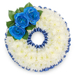 A bespoke funeral tribute crafted into the distinct shape of the numeral '0', shown against a clean white background so every detail reads clearly to the eye. The entire figure is densely covered with hundreds of small white spray chrysanthemum florets, their finely textured petals layered like a soft, snow-white cushion that suggests quiet and comfort. Around both the outer rim and the inner aperture of the zero a deep royal-blue trim defines the silhouette; the border could be a pleated satin ribbon or a ring of carefully dyed blooms, its scalloped finish echoing the ruffled edges of the chrysanthemums and lending the piece a formal, ceremonial edge. Nestled along the upper-left curve is a small cluster of three vivid royal blue roses, petals unfurling from tight centers and catching the light with a subtle silk-like sheen. Lush, dark green foliage tucks discreetly behind these roses, offering contrast and a shaded, natural depth that anchors the composition. Soft, neutral studio lighting highlights the chrysanthemums' tactile surface and the blue roses' saturated hue without harsh shadows, conveying serenity rather than drama. The overall mood is one of respectful remembrance: cool, composed, and meticulously balanced in scale and colour. This personalised number tribute is suitable for remembering an age or significant year at local memorials in Mill Hill Village or services near Mill Hill Broadway, offering families a quiet, dignified expression of loss and love. The arrangement's textures, tones, and careful craftsmanship make its intent unmistakable-a gentle, visual benediction for those gathered to remember.