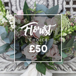 A hand-tied bouquet of soft-blush garden roses and cool, silvery eucalyptus presented in gentle, natural daylight. The rounded rose heads unfurl in layers of pale pink, their velvet petals catching a diffuse morning glow, while clusters of bright white berries - snowberry or hypericum-like - punctuate the composition with crisp highlights. Fine sprays of tiny white waxflower or astrantia weave through the arrangement, creating an airy, wildflower feel that contrasts with the denser rose forms. Taller, slender green-and-white spikes peek from the left and right edges, suggesting snapdragon or similar vertical accents that give the bouquet a relaxed, cottage-garden silhouette. Texturally the design is thoughtful: the cool, smooth leaves of eucalyptus sit alongside waxy green foliages and the soft, yielding petals of each rose so you can almost imagine the scent of crushed leaves and sweet blooms. A cream satin ribbon gently binds the stems, hinting at a bespoke hand-tied finish ready to rest on an antique cream mantle or console. In the photograph a delicate white square frame and clear text overlay name this arrangement as a 'Florist Choice' priced at £50, a curated selection that balances simplicity and luxury. This bouquet reads as comforting and refined, suited to small celebrations - a milestone birthday, a thank-you, or to welcome someone home in Mill Hill. The overall impression is one of calm elegance and meticulous craft, as if assembled by a local florist who knows how to combine texture, scent and seasonality for both everyday joy and intimate moments.