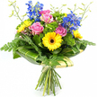 Set against a spotless white background, this hand-tied bouquet glows with fresh colour, like a bright splash of flowers carried along Mill Hill Broadway on a clear afternoon. At the centre, several pink roses open fully, their petals layered in soft, rounded spirals that suggest tenderness, admiration, and heartfelt sentiment. Interwoven with them, yellow gerbera daisies bring a burst of cheerful light, each flower displaying a perfect circle of sleek petals surrounding a pronounced dark brown centre, giving the bouquet a playful focal point. Rising above these warm tones, tall, upright stems of rich blue delphinium or larkspur lend a cool, elegant contrast; each vertical spike bears multiple delicate blossoms, adding height and a slightly wild, garden-meadow feel. The bouquet is richly cushioned with a variety of greenery. Fine, feathery fern fronds soften the outer edges, while bright green, textured filler foliage tucks between the blooms, building depth and a plush, abundant look. Around the base of the flowers, broad, glossy dark green leaves-some finely striped in a lighter hue-are wrapped to form a smooth, curved collar, giving the design both structure and a polished, modern edge. From the top, slender, pale green stems tipped with tiny unopened buds arc gently upward, providing lightness and a sense of ongoing growth. At the lower end, the natural stems are cleanly gathered and wrapped in a pale cream or soft green paper or fabric, secured with a simple tie that emphasises its hand-crafted nature. The overall effect is joyful, uplifting, and versatile, ideal for celebrating a birthday, marking a special achievement, or sending a thoughtful surprise to someone in Mill Hill, from homes near Mill Hill East station to offices around the Broadway. Flowers Mill Hill could easily create and deliver such a bouquet to brighten any local day.